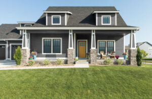 attractive gray home with stone pillars on either side of a stunning wood entry door